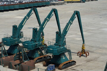 Tree green tracked excavators form Mantsinen company use for handling of scrap are parked in port, awaiting loading and discharging scrap form ships in cargo terminal. 