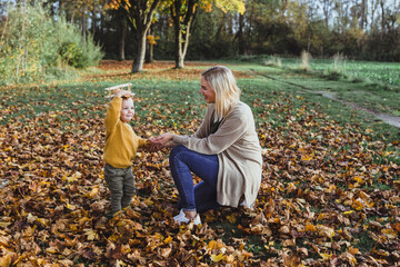 Happy mother looking at boy holding toy airplane on head in autumn