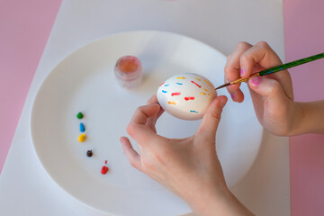 A ten-year-old girl decorates an egg for Easter. Acrylic paints and brush. Close-up.