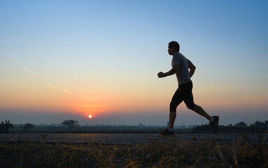 Fototapeta premium Asain man jogging on country road with sunrise background.