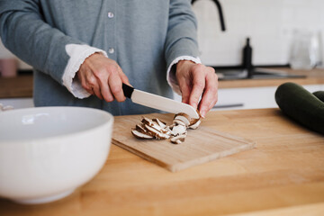 Hands of woman cutting mushrooms with knife in kitchen