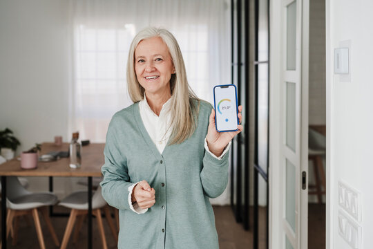 Happy woman showing thermostat mobile app on device screen at home