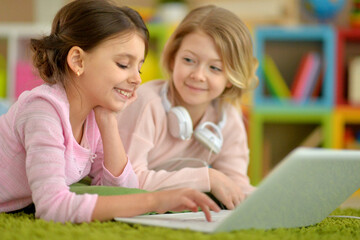 Two pretty little girls lying on floor and using laptop