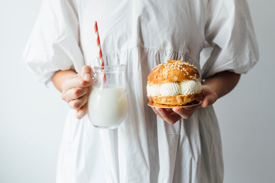 Woman with milk jar and small cake in front of white wall