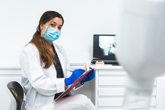 Young dentist wearing surgical mask sitting with clipboard in clinic