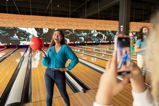 Woman photographing friend through smart phone in bowling alley