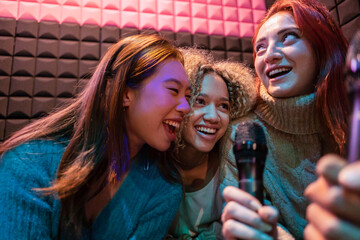 Happy young women singing karaoke in microphone at amusement arcade