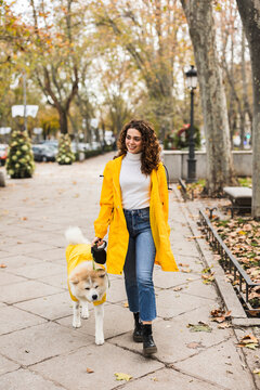 Smiling Young Woman Walking With Dog On Footpath