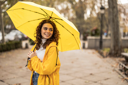 Happy beautiful woman with yellow umbrella standing at footpath