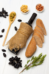 Bottle of wine and a French baguette. Olives on a wooden spoon. Sprig of black grapes and rosemary.