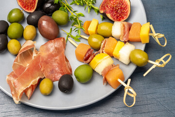 Skewers with olives, cheese, and melon on a gray plate.