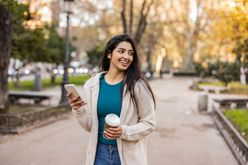 Thoughtful smiling young woman with smart phone standing at park