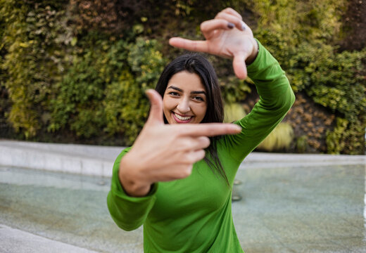 Smiling woman making frame with fingers in front of vertical garden