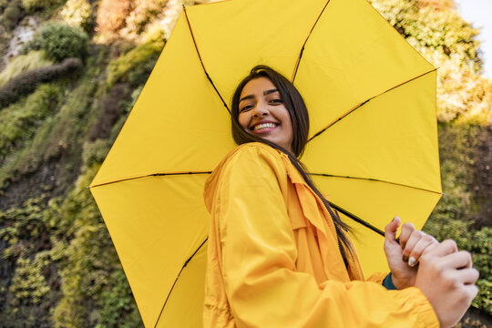 Smiling young woman holding yellow umbrella in front of vertical garden