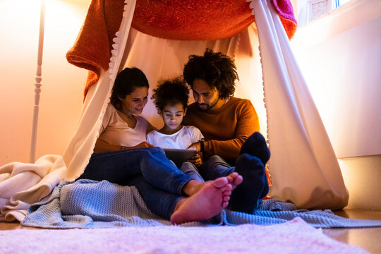 Mother and father using tablet PC with daughter sitting in tent at home