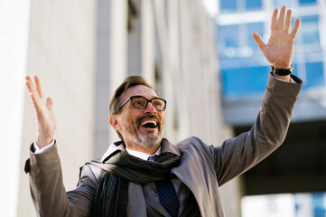 Cheerful mature businessman with hand raised outside office building