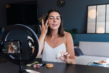 Young woman applying make-up and recording tutorial on mobile phone
