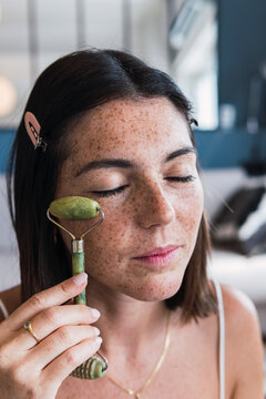 Young woman with eyes closed massaging face using jade stone roller