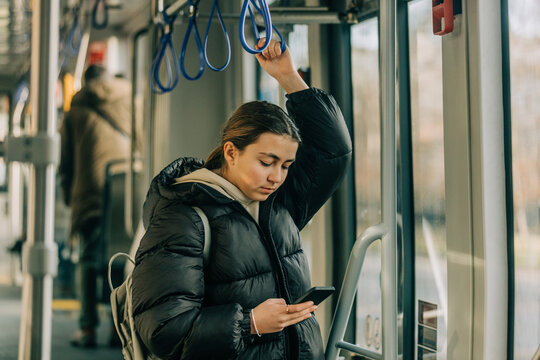 Teenage girl using smart phone standing in tram