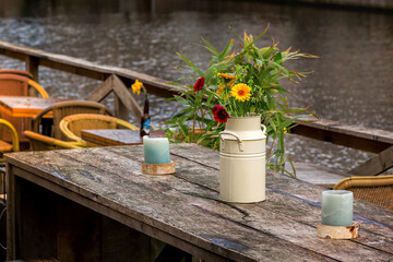 Cozy street cafe wooden table with flowers in vase. Outdoor restaurant decor with candles in...