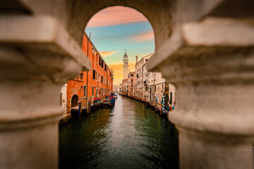 Characteristic canal of Venice at sunset with famous crooked bell tower from bridge gap