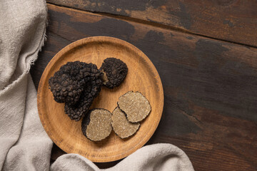 Whole and sliced black truffles mushroom on wooden plate on dark brown table, flat lay, copy space. - Powered by Adobe