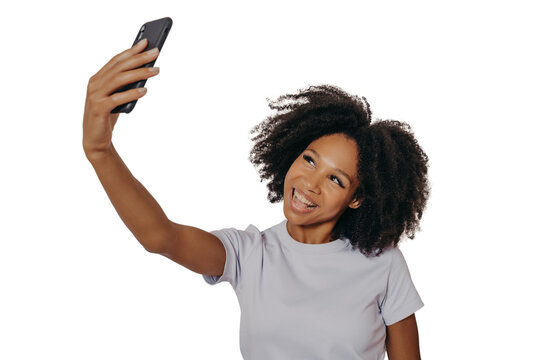 Cheerful young african woman with curly hair taking selfie on her modern mobile phone