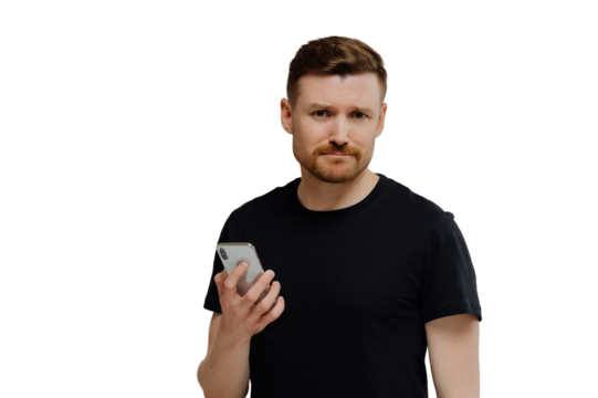 Upset dissatisfied bearded young man holds modern smartphone waits for call frowns face dressed in black casual t shirt isolated over white background being worried about recent terrifying news