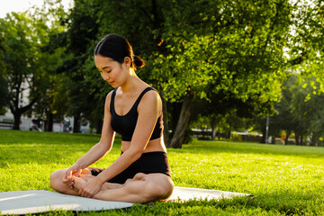 Young brunette asian woman practicing yoga during workout in park