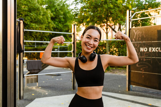 Young asian woman smiling and showing her biceps on playground