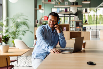 Young businessman in formal wear using laptop and cellphone at office