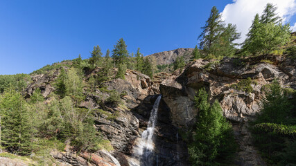 Fototapeta na wymiar Lillaz waterfall (Cascate di Lillaz) splashes alpine water and breaks through crevice of granite rocks in Parco Nazionale Gran Paradiso, Aosta valley, Italy