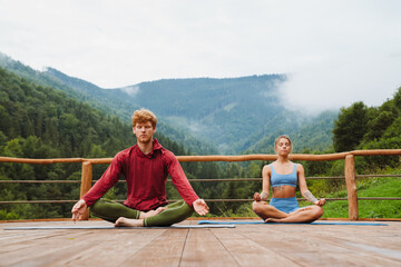 Young white man and woman practicing yoga on fitness mats in forest