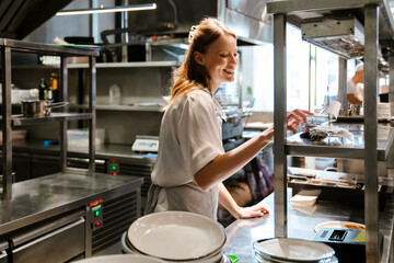 Young woman holding order receipts while working in restaurant kitchen