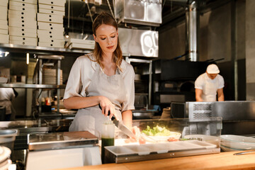 Fototapeta na wymiar Young white chef woman cooking while working in restaurant kitchen