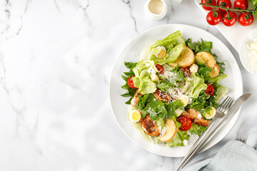 Caesar salad with roasted chicken meat, tomatoes, croutons and parmesan cheese in white plate.