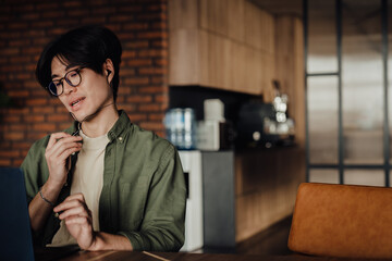 Asian business man talking on video call with earphones while sitting in office