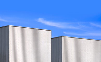 Fototapeta na wymiar Two corrugated metal industrial warehouse building against blue sky background in perspective side view