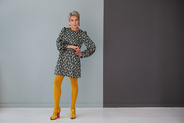 Mature fashion model short hair wear short print dress and colorful yellow tights, high-heeled...