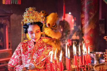 Woman traditional dress in Chinese shrine light up candle joss stick pray in temple lion stay behind
