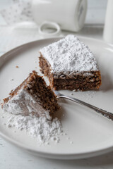 Flat chocolate cake with almonds, traditional italian torta caprese on a white plate