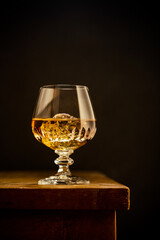 Glass of scotch whiskey and ice on old wooden table over black background with copy space