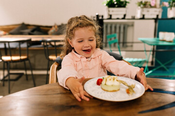 Happy surprised little girl sitting in cafe with healthy desert. The child sits at a table in a cafe and is happy. A happy birthday girl with dessert. 