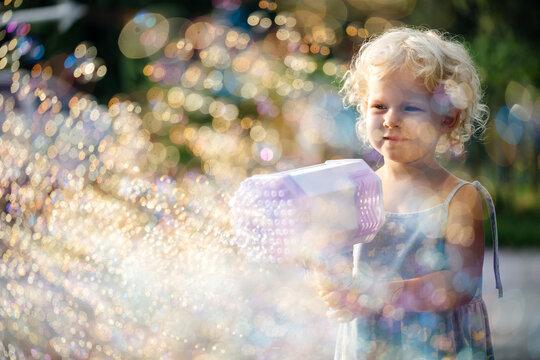 Portrait of a girl through soap bubbles on the street in summer.