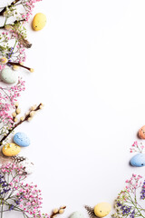 Border with Easter composition with spring flowers and colorful quail eggs over white background. Springtime and Easter holiday concept with copy space. Top view - 561766518