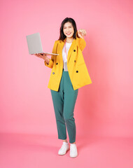 Full length image of young Asian bussinesswoman holding laptop on background