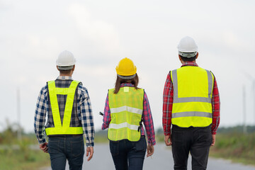 A behind-the-scenes photo of a team of 3 engineers or architects wearing uniforms and helmets. walk to the path ahead Look at the power and bright future and unity together. on one street.