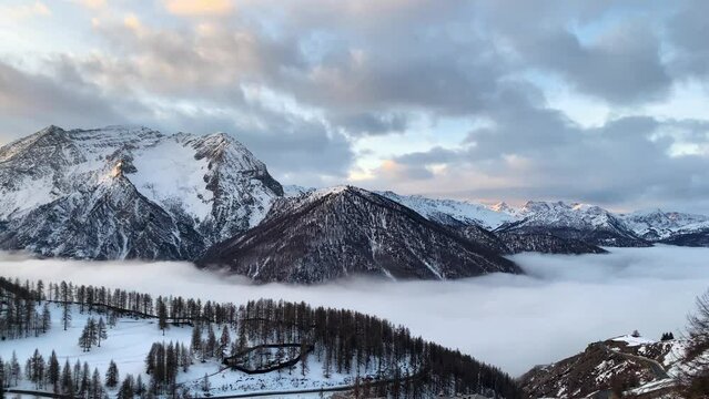 A white and soft cloud fill completely the valley in a winter day. All around there are snow capped mountain lighted from a warm morning sun. pan camera movement