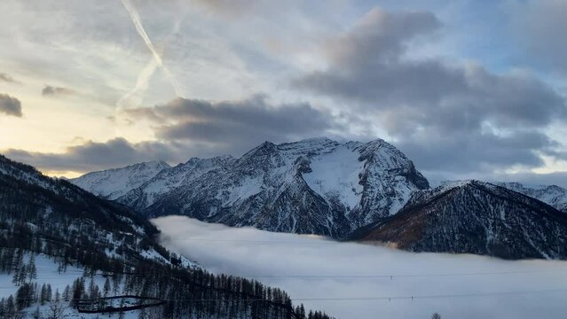 A white and soft cloud cover completely the valley in a winter day. All around there are snow capped mountain lighted from a warm morning sun.