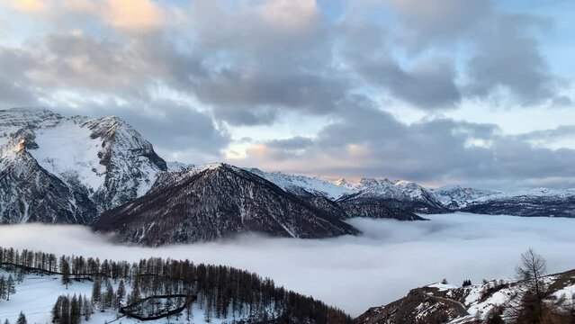 A white and soft cloud fill completely the valley in a winter day. All around there are snow capped mountain lighted from a warm morning sun. pan camera movement